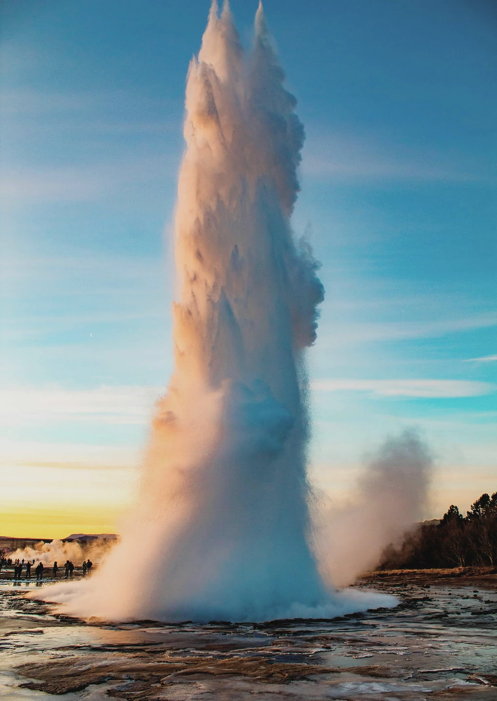 A tall geothermal geyser erupting against a blue sky