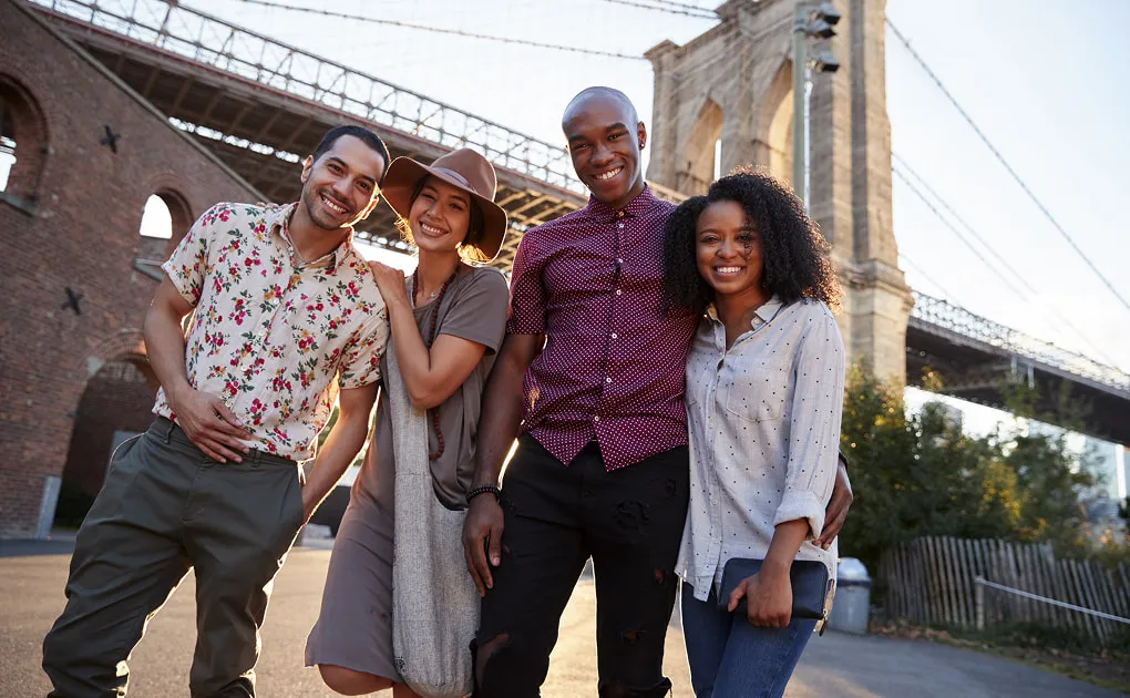 Four friends standing together beneath a city bridge
